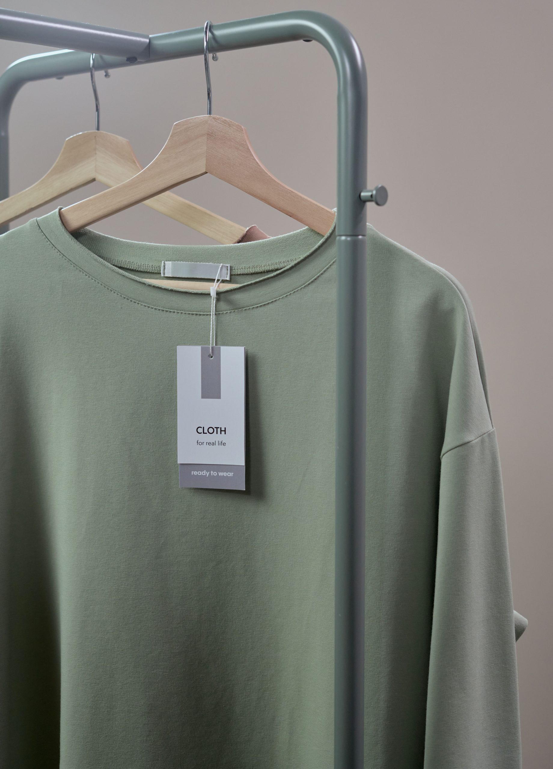 Close-up of a green shirt on a hanger with label tag on a minimalist clothing rack.